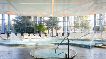 Un espace piscine comprenant un jacuzzi, des chaises longues et une vue sur les arbres à travers de grandes fenêtres.