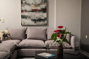 A modern living room with a grey sofa, a coffee table with a book, and a potted plant with red flowers.