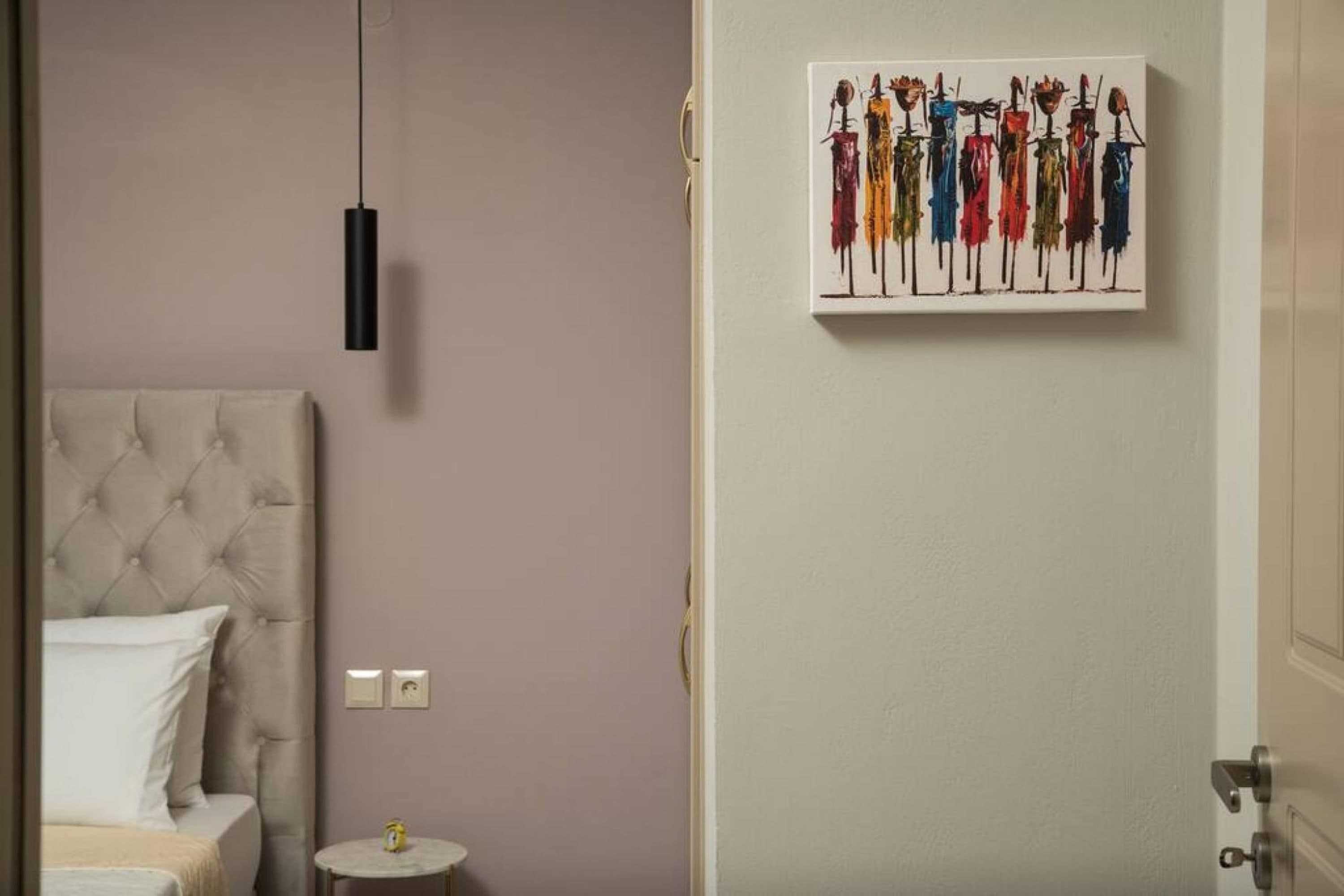 A bedroom with a tufted headboard, a bedside table, and a wall-mounted artwork depicting colorful figures.