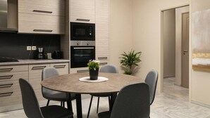 A modern kitchen with built-in appliances, a dining table with chairs, and a potted plant.