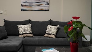 A grey sofa with patterned cushions, a red potted plant, and a painting on the wall.