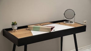 A small, modern desk with a wooden top and black legs, featuring a potted plant, a book, and a round mirror.