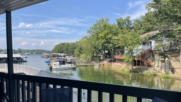 A view from a balcony overlooking a river with boats, a dock, and a house with a wooden staircase.