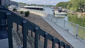A riverside walkway with a wooden bench, a white fence, and boats docked along the river.