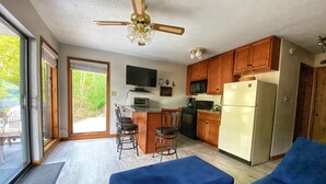 A compact kitchen with wooden cabinets, a microwave, a stove, and a refrigerator. There is a dining area with a table and chairs, and a large window providing a view of the outdoors.