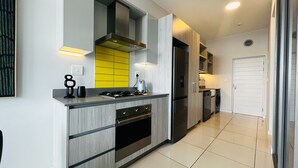 A modern kitchen with a built-in stove, oven, and dishwasher, featuring light wood cabinetry and a yellow backsplash. - Modern 1 Bed Apartment in Trendy Rosebank (Johannesburg)