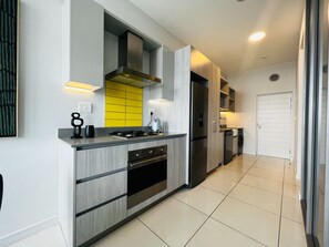 A modern kitchen with a built-in stove, oven, and dishwasher, featuring light wood cabinetry and a yellow backsplash.