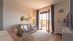 A modern hotel room with a sofa, a desk, a dresser, and a large window with curtains. - Le Orchidee by Wonderful Italy (Sanremo)