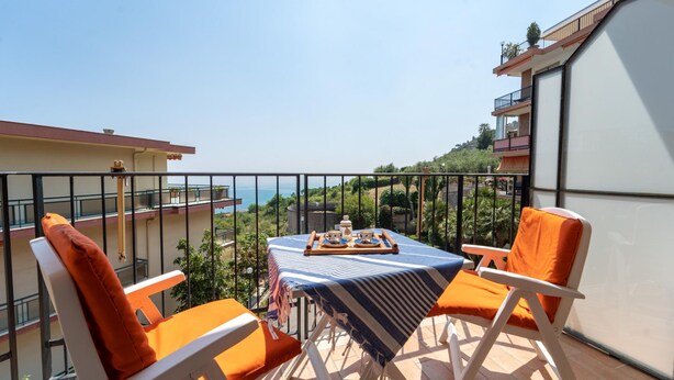 A balcony with two white chairs and a table, overlooking a scenic view of the sea and hills. - Le Orchidee by Wonderful Italy (Sanremo)
