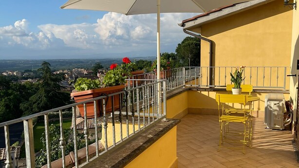 Een balkon met een gele muur, een witte parasol en uitzicht op de stadsgezicht.
