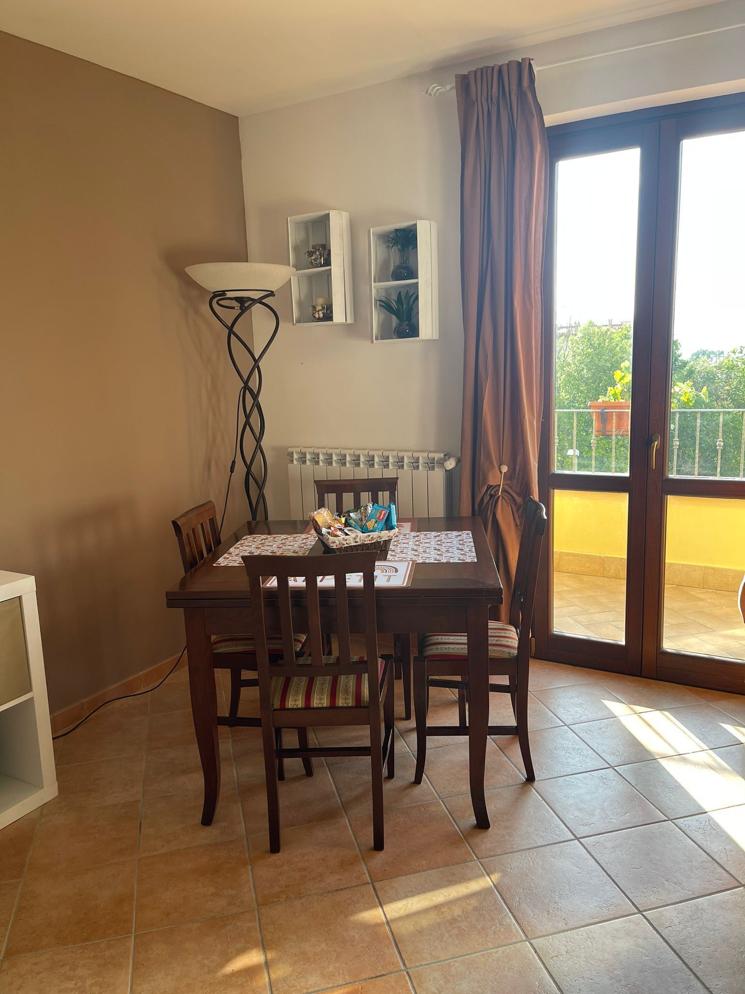 A dining area with a table set for four, a radiator, and a view of a balcony with a railing.