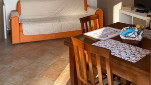 Een woonkamer met een bank, een eettafel met stoelen, een televisie en een aan de muur hangend schilderij.
