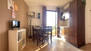 Een ruimtelijke zithoek met eethoek, kitchenette en een televisie op een witte kast.