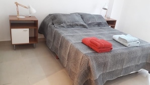 A neatly made bed with a grey blanket, a red towel, and a white towel on the side. There are two bedside tables with lamps, one on each side of the bed. - Excelente Ubicación (Ushuaia)