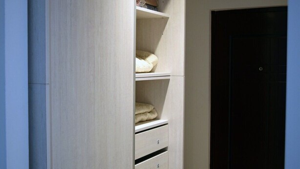 A closet with shelves and drawers, a dark door, and a light-colored wall. - Excelente Ubicación (Ushuaia)