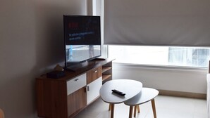 A modern living room with a flat-screen TV on a wooden cabinet, a small table, and a window with a blind. - Excelente Ubicación (Ushuaia)