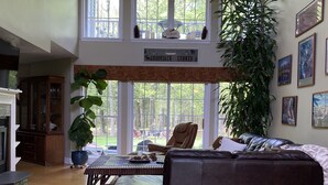 A spacious living room with a large window, a ceiling fan, a fireplace, and a dining area with a table and chairs. - Privacy yet close to downtown Saratoga (Greenfield Center)