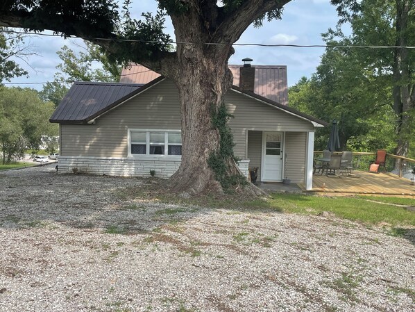 A small house with a stone foundation, a metal roof, and a wooden deck. - Nana's House located in the MO Ozarks close to many rivers for floating. (Houston)