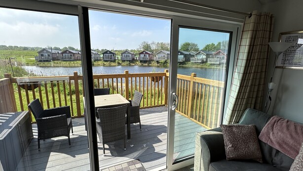 En balkong med ett bord och stolar, en soffa och utsikt över hus på andra sidan en vattenyta.