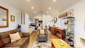 A modern living room with a sofa, a dining table, and a kitchen in the background. - Stunning Coastal Lodge - Sleeping 4 in 2 Bedrooms - Pool and Beach Access Included. (Lakeside - The Meadows)