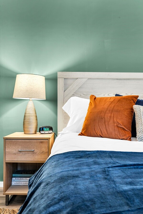 A neatly made bed with a blue blanket, a wooden nightstand with a lamp and a digital clock, and a green wall. - Pine and Eagle- Family & Dog Friendly Great Views (Sebago)