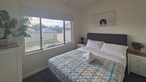 Une chambre à coucher avec un lit, une fenêtre, une table de chevet, une lampe et un tableau accroché au mur.