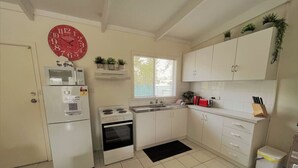 Une cuisine de taille réduite avec des meubles blancs, un four à micro-ondes, une cuisinière et une horloge rouge.