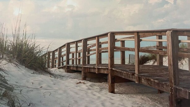 A wooden boardwalk leading to a beach with sand dunes and sparse vegetation.