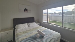 A bedroom with a bed, a nightstand, a window with a view, and a wall-mounted picture.