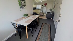 A compact kitchen with modern appliances, a dining area with a long table and chairs, and a small seating area with a sofa.