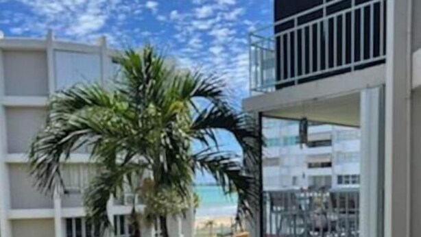 Un edifici de diverses plantes amb balcons, una palmera i vista a la platja.