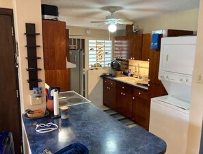 Eine kleine Küche mit blauer Arbeitsplatte, Holzschränken, einem weißen Kühlschrank und einem Deckenventilator.
