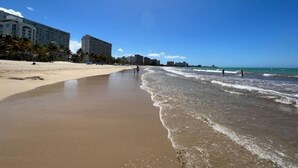 Una platja amb sorra, algunes persones i edificis al fons.