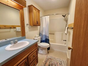 Une salle de bain avec un meuble-lavabo en bois, des toilettes, une baignoire et une douche.