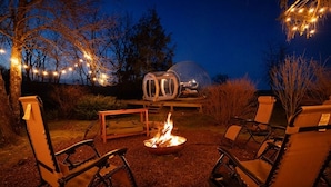An outdoor seating area with chairs and a fire pit, surrounded by trees and string lights.