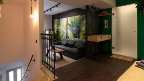 Una sala de estar moderna con piso de madera oscura, un sofá negro y un gran mural tropical en la pared.