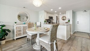 A modern kitchen with white cabinetry, a dining area with wicker chairs, and a chandelier. - Amelia Surf & Racquet Club Condo 5th Floor Oceanview Pools Tennis Court Sleeps 4 (Fernandina Beach)