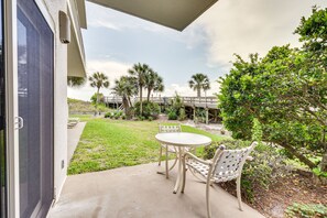 An outdoor patio with a table and chairs, a covered area, and a view of a bridge and palm trees. - Beachfront Vacation Rental w/ Hot Tub, Pool, Sauna (Miramar Beach)