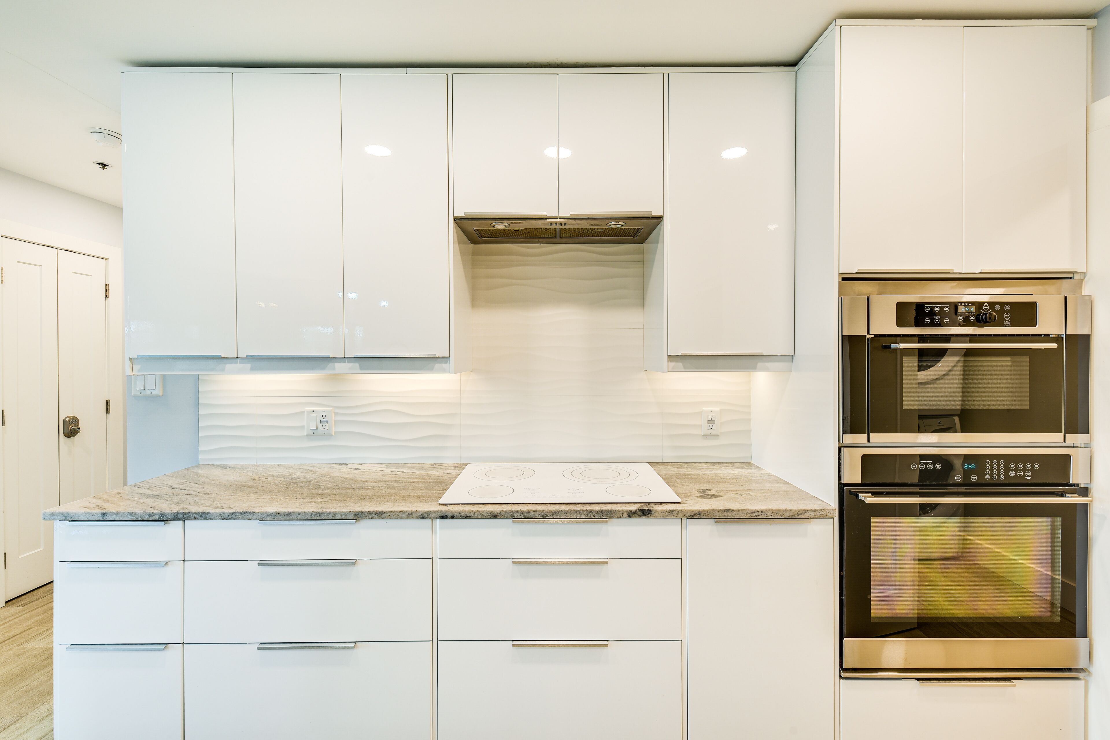 Een moderne keuken met witte kastjes, een marmeren werkblad en roestvrijstalen apparatuur, waaronder een oven en een geïntegreerde kookplaat.