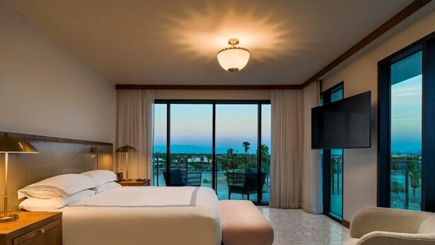 A hotel room with a bed, a desk, a chair, a TV, and a large window with a view.