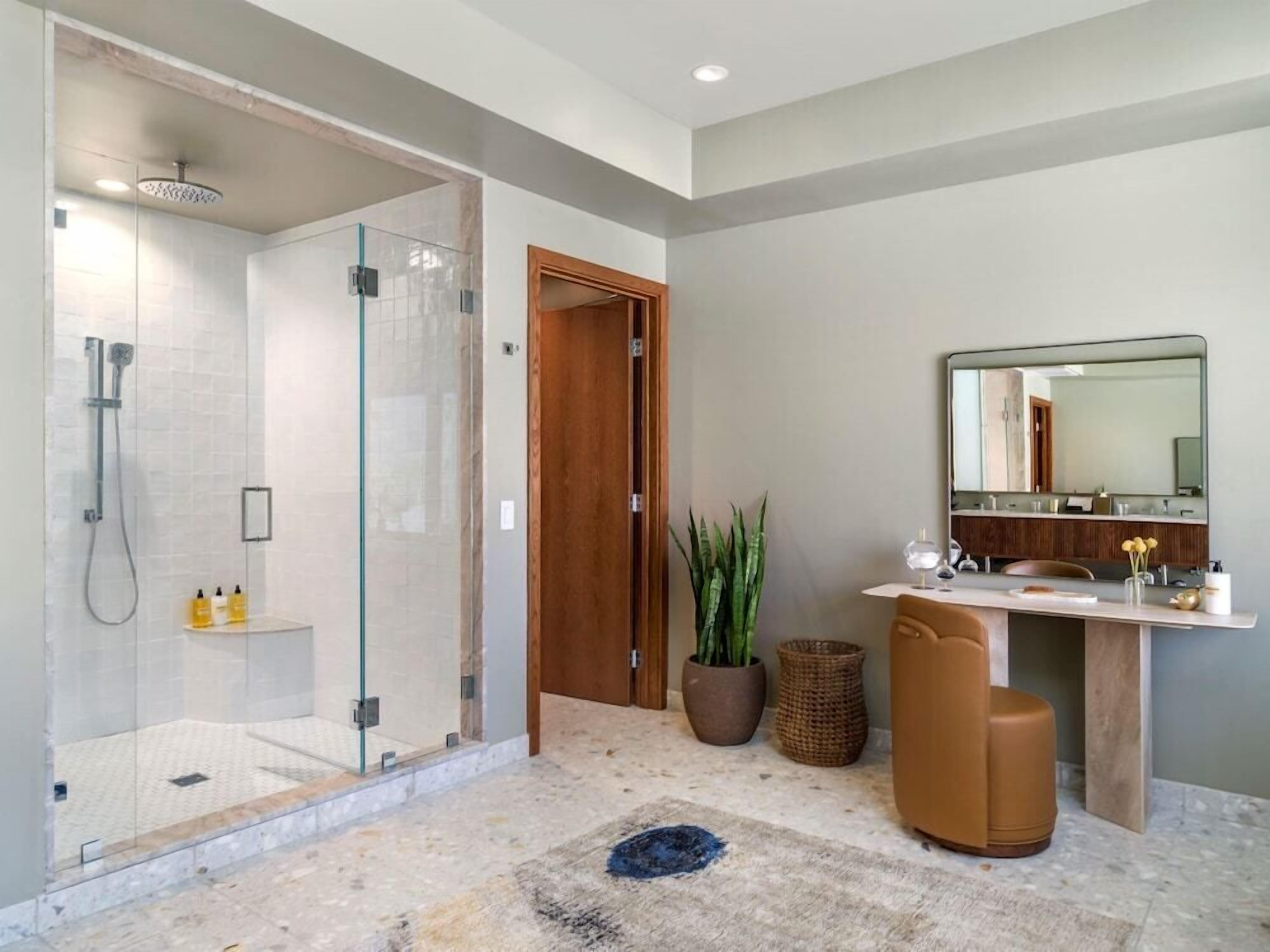 Ein modernes Badezimmer mit einer gläsernen Dusche, einer Holztür, einem großen Spiegel und einer kleinen Sitzecke.