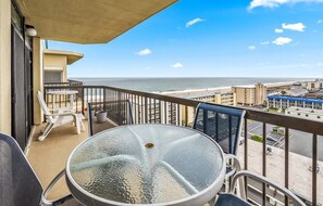 Varanda com mesa e cadeiras de vidro, com vista para a praia e para o horizonte da cidade.