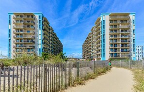 A beachfront hotel with multiple balconies and a sandy path leading to the beach.