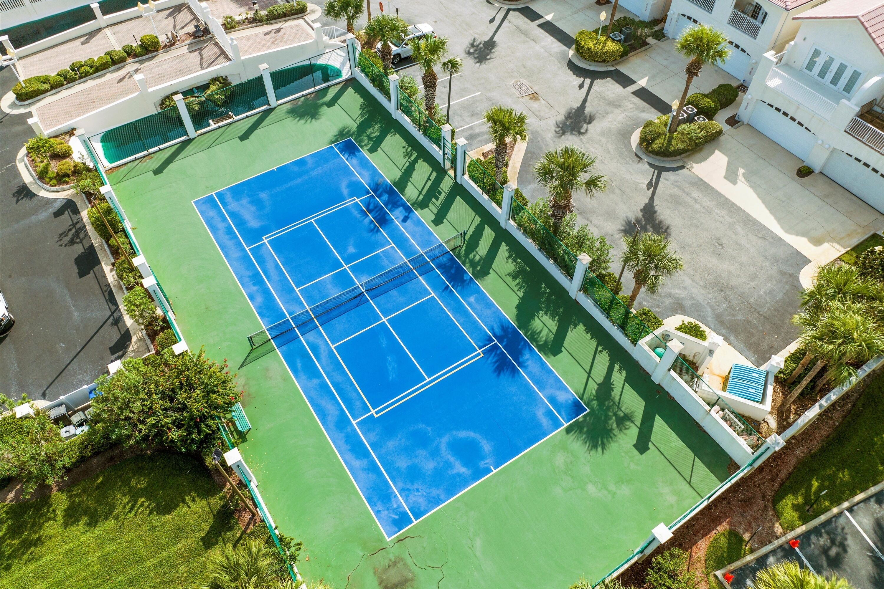 Une vue aérienne d’un court de tennis entouré de verdure et d’immeubles résidentiels.