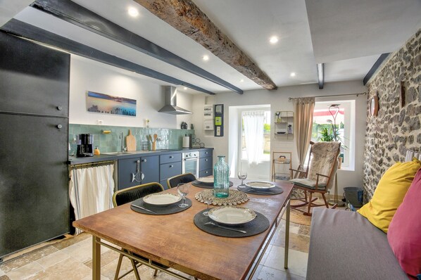 A dining area with a wooden table set for four, a kitchen with modern appliances, and a stone wall.