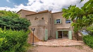 A rustic building with a stone facade, green shutters, and a stone staircase leading to a door.