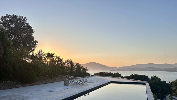 A swimming pool with a view of the sea and mountains during sunset.