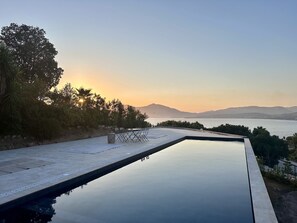 A swimming pool with a view of the sea and mountains during sunset.