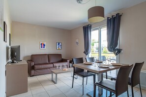 Una sala de estar moderna con un sofá de cuero marrón, una mesa de comedor con sillas, un televisor sobre un mueble bajo y obras de arte en las paredes.