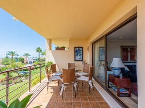 A balcony with wicker chairs and a table, a potted plant, and a view of the landscape. - Los Pinos, 3 bedroom apartment in Los Arqueros (Benahavis)